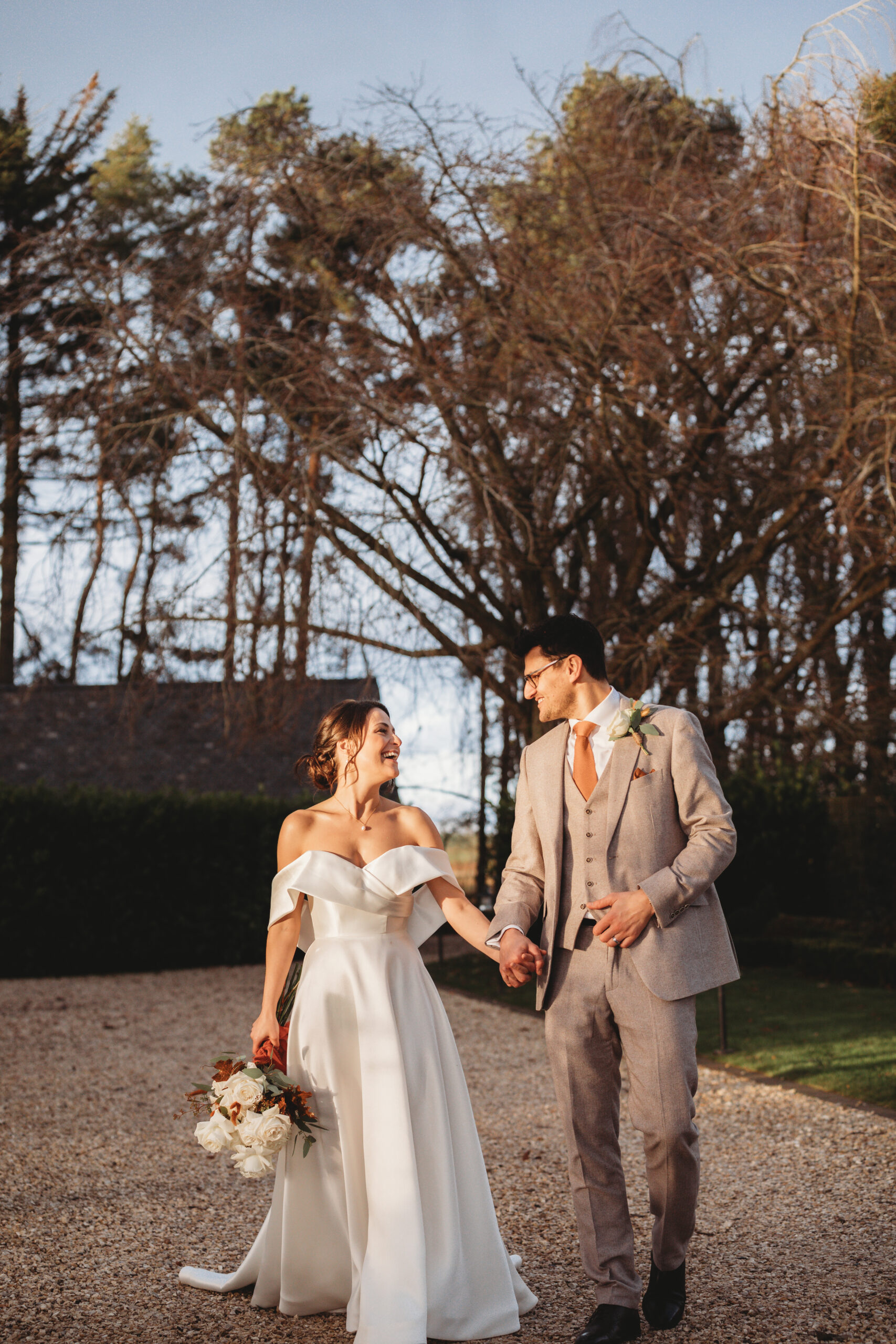 Bride and groom walk holding hands, golden hour sunset photo session